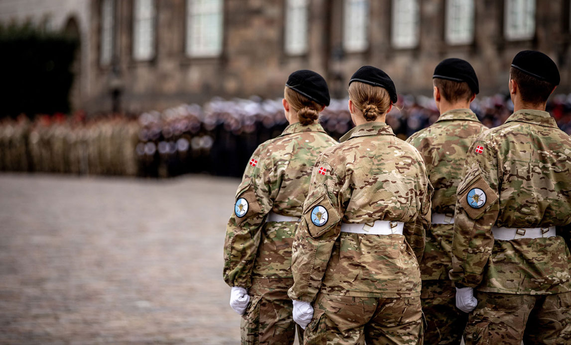 Parade ifm. Flagdagen på Christiansborg Slotsplads. I forgrunden ses to kvindelige og to mandlige soldater i uniform. Det står med ryggen til.